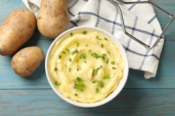 Tasty mashed potato with green onion in bowl and raw vegetables on light blue wooden table, flat lay