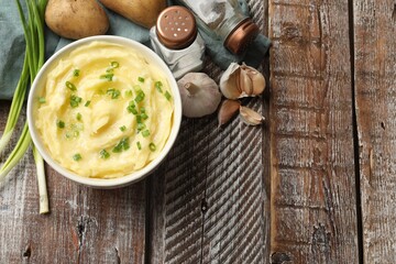 Tasty mashed potato with green onion in bowl, spices and raw vegetables on wooden table, flat lay. Space for text