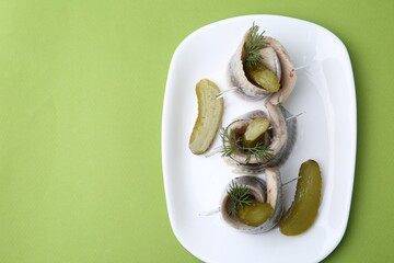 Delicious herring rolls with pickles and dill on light green table, top view. Space for text