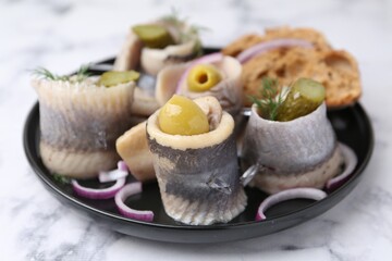 Delicious herring rolls with olives, pickles, dill, onion and bread pieces on light marble table,...