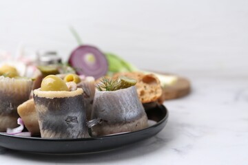 Delicious herring rolls with olives, pickles, dill and onion on light marble table, closeup. Space for text