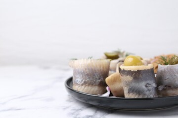 Delicious herring rolls with olives, pickles and dill on light marble table, closeup. Space for text