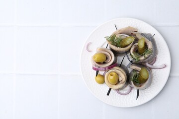 Delicious herring rolls with olives, pickles, dill and onion on light tiled table, top view. Space...