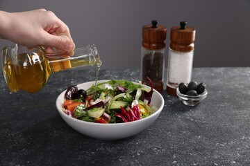 Woman pouring oil onto salad at dark textured table against grey background, closeup