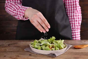 Woman salting tasty salad at wooden table, closeup