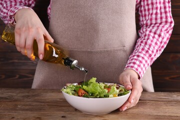Woman pouring oil onto tasty salad at wooden table, closeup
