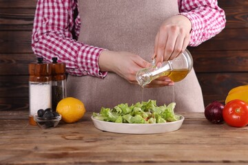 Woman pouring oil onto tasty salad at wooden table, closeup
