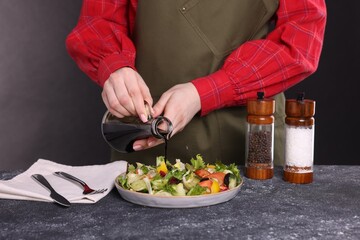 Woman pouring balsamic vinegar onto tasty salad at dark textured table, closeup