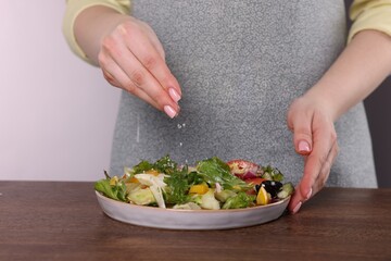 Woman salting tasty salad at wooden table against white background, closeup