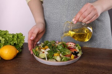 Woman pouring oil onto tasty salad at wooden table against white background, closeup