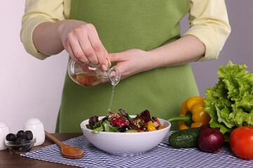 Woman pouring oil onto tasty salad at wooden table against white background, closeup