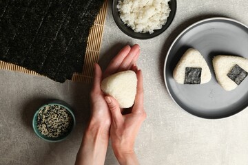 Woman making tasty onigiri (Japanese rice balls) at light table, top view