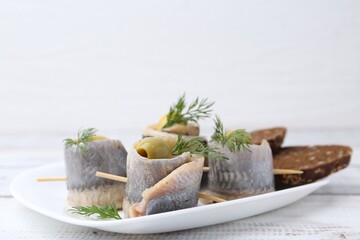 Delicious herring rolls with olives, dill and bread on white wooden table, closeup