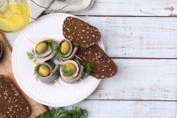 Delicious herring rolls with olives served on white wooden table, flat lay. Space for text