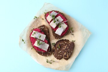 Tasty sandwiches with herring and horseradish sauce on light blue background, top view