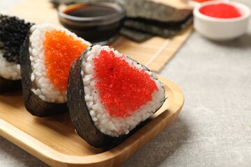 Tasty tobiko onigiri (Japanese rice balls) served on light grey table, closeup. Space for text