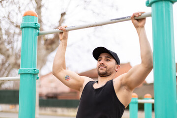 Strong man doing pull-ups on fitness bar at park.