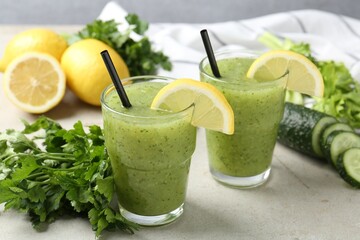 Healthy parsley smoothie in glasses, leaves, cucumber and lemon on light textured table against grey background, closeup