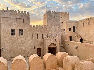 Nizwa Fort in Oman at sunset - Ancient mud brick fortress with crenellated walls, watch towers and courtyard under dramatic cloudy sky