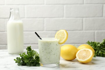 Healthy parsley drink in glass, leaves and lemons on white marble table
