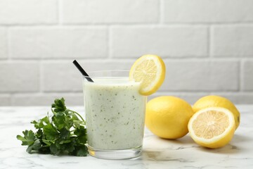 Healthy parsley drink in glass, leaves and lemons on white marble table