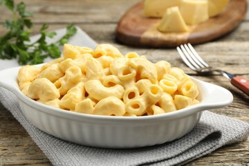 Delicious pasta with cheese sauce, parsley and fork on wooden table, closeup