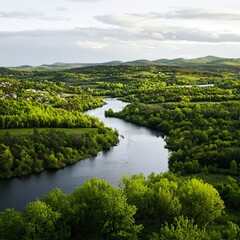 Fototapeta premium Serpentine river meandering through lush green valley, village in distance. Perfect for travel brochures