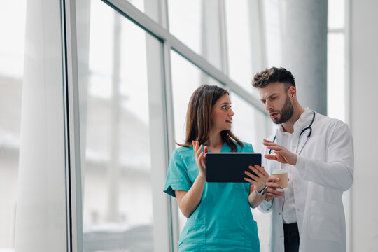 Doctors using tablet and discussing diagnosis in hospital corridor