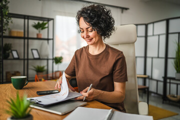 mature curly hair woman work from home write details on clipboard