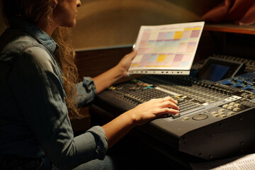Hand of female journalist with broadcast schedule sitting by sound mixing console and moving knobs...