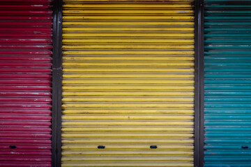 A close-up view of a dilapidated garage door in red, yellow, and green tints with black iron bars dividing it.