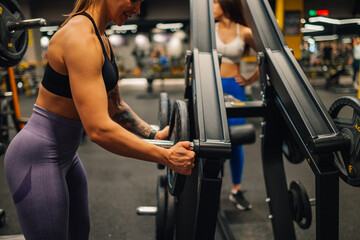 Strong woman adding weights to barbell in modern gym