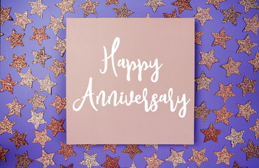 Happy Anniversary text on paper card with star glitter decoration flat lay on purple background
