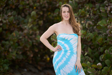 Fototapeta premium Attractive young woman in blue sundress stands in front of vegetation