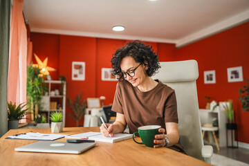 focused mature woman work from home and take notes in notebook
