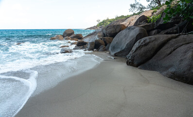 Tropical beach with soft sand, crashing waves, and large granite boulders