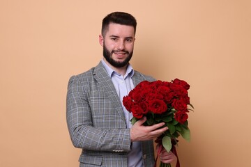 Happy man with bouquet of red roses on beige background