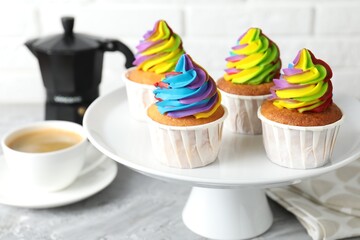 Delicious cupcakes with colorful cream and cup of coffee on grey table, closeup