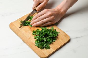 Woman cutting fresh parsley at white table, closeup