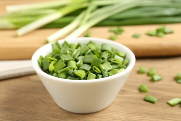 Cut fresh green onions in bowl on wooden table, closeup
