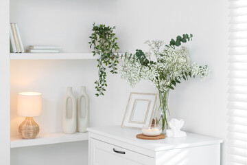 Bouquet of beautiful gypsophila flowers and eucalyptus branches in vase surrounded by decorative elements on chest of drawers indoors