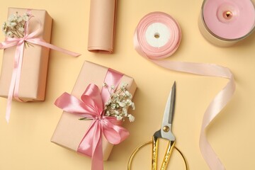 Florist. Boxes, flowers, ribbon, burning candle and scissors on beige background, flat lay