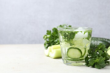 Healthy drink with parsley, cucumbers and celery on light table, space for text