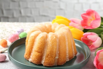 Delicious bundt cake, Easter eggs and tulips on table, closeup