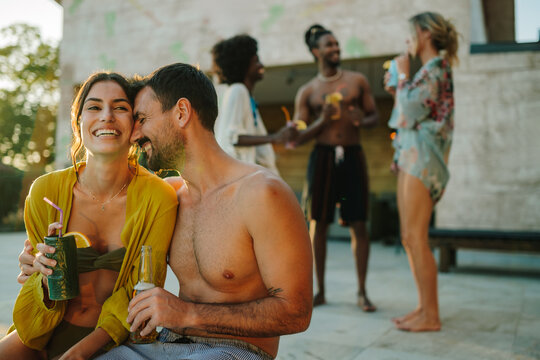 Happy couple enjoying drinks at poolside party with friends - Powered by Adobe