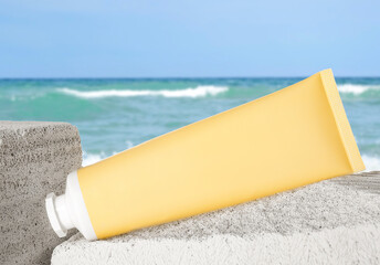 Tube of sunscreen product on beach near ocean