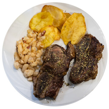 Grilled beef with spices and herbs with potatoes and beans on a white plate. Meat dish according to a traditional Spanish recipe. Isolated over white background