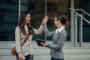 Two businesswomen giving high five celebrating success outdoors