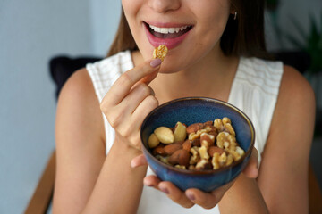 Young woman eating mix of nuts dried fruits from bowl at home