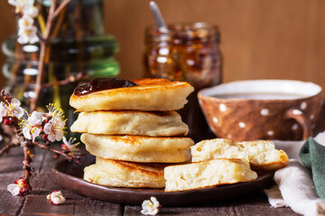 Lenten yeast pancakes with plum jam and tea, and a bouquet of blooming apricot branches on a wooden table.